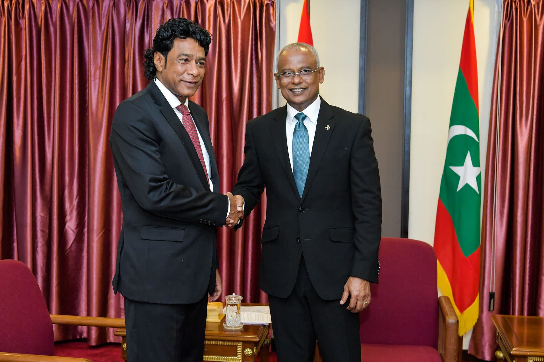 Nando Bodha serre la main du président des Maldives, Ibrahim Mohamed Solih, devant les drapeaux maldiviens